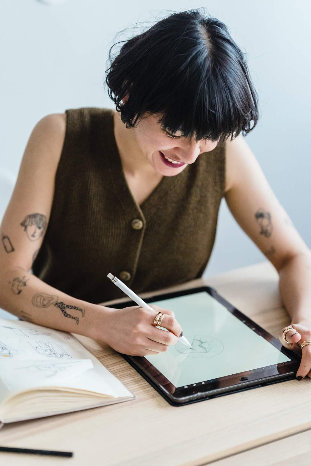 Lady with tattoos on hand smiling and drawing on Ipad