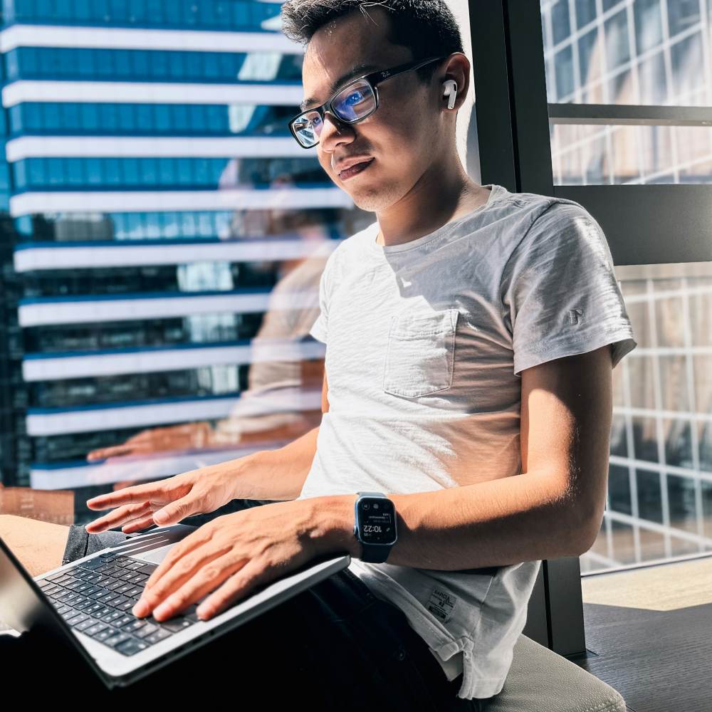 a man sitting in front of a window using a laptop